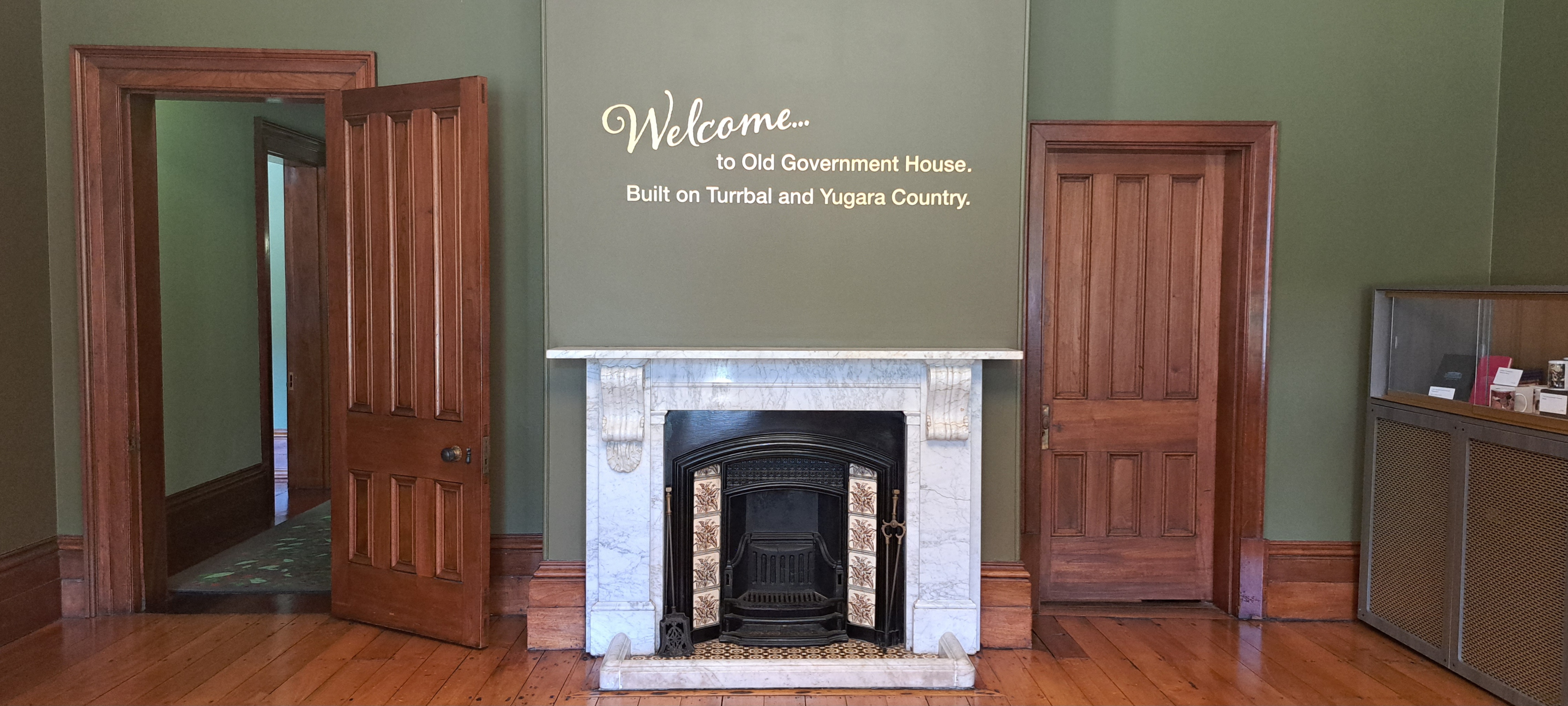 A marble fireplace in Old Government House. Above it are the words 'Welcome to Old Government House. Built on Turrbal and Yugara Country.