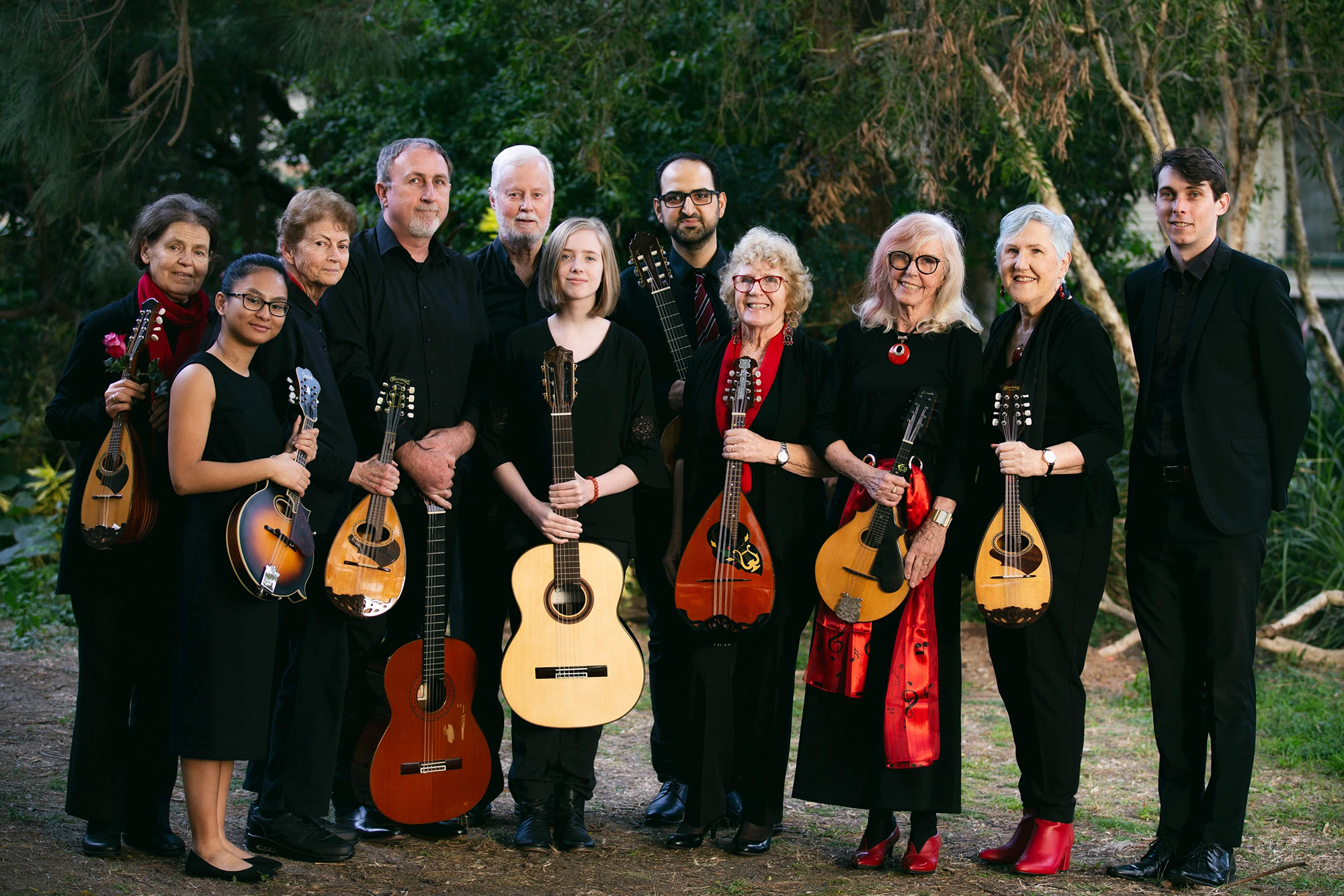 Photo of 11 musicians holding instruments standing in front of trees